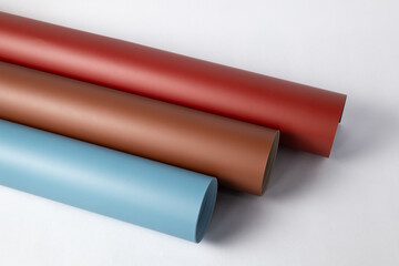 Seamless background rolls in matte red, earthy brown, and pale blue, diagonally stacked on a clean white surface for studio photography, crafting, or design