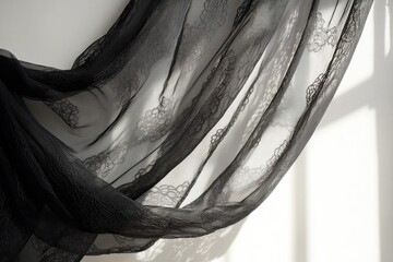 Elegant black sheer lace fabric, draped beautifully, showcases delicate floral patterns against a white background with captivating natural light and shadows.