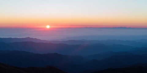 Naklejka premium Sunrise illuminating mountain ranges and clouds in a layered landscape