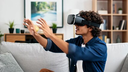 Happy young man using virtual reality headset at home while sitting on sofa and interacting with VR experience. - Powered by Adobe