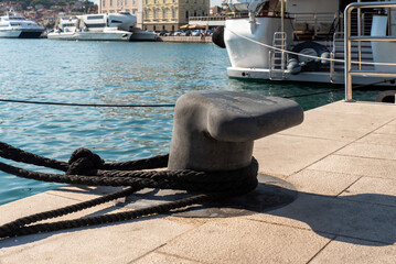 Metal mooring bollard with black ropes on marina pier