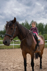 Obraz premium Cute little girl riding a horse outdoors. Pet therapy. Hippotherapy for young children, therapy after many serious diseases.