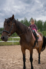 Cute little girl riding a horse outdoors. Pet therapy. Hippotherapy for young children, therapy after many serious diseases.