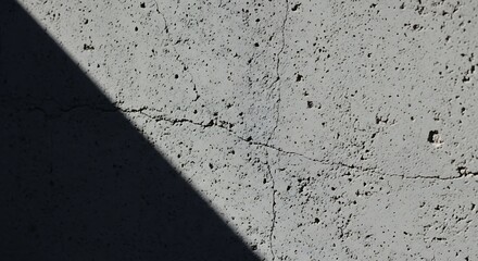 Close up view of a textured concrete wall with cracks and a shadow casting across the surface
