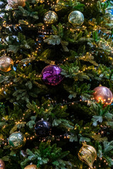 Vertical festive background of Christmas tree with pink and gold balls and garland lights, selective focus
