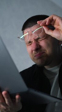 A man working on a computer takes off his glasses and squints from eye strain.
A man with poor eyesight is working on a laptop.
A man's eyes are watering from working on a computer.
