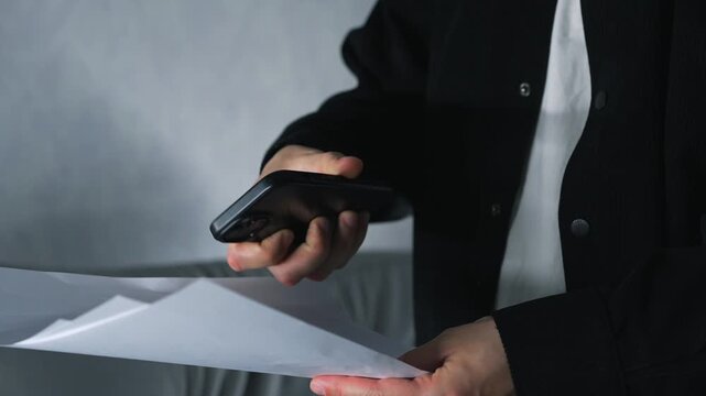 A businessman holding paper documents and a mobile phone takes a photo of text on the paper while standing in a dark room.
Information and digital technology.
Photography, paper, business, camera, pho
