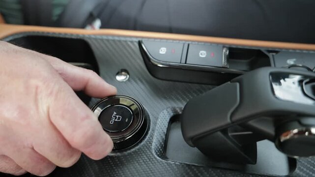 A closeup image shows a hand skillfully operating a control dial located in the interior dashboard area of a car