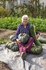 Elderly woman is happy with her pumpkin crop, sits  and smiles
