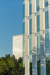 Obraz premium Contemporary office building exterior with vertical glass panels against a clear blue sky. Suitable for illustrating urban architecture, business environments, and modern city development concepts.