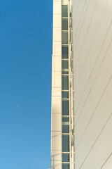 Tall modern building with white panels and vertical windows, set against a clear blue sky. Suitable for architecture, construction, or urban design themes in editorial or commercial use.