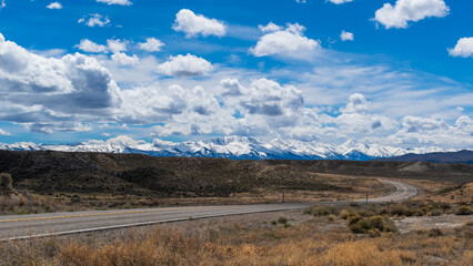 Desert Road Leading to Snow-Capped Mountains Under Partly Cloudy Sky, Nevada in Spring