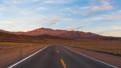 Curving Desert Road Leading to Reddish Mountains Under Pale Blue Sky with Pink-Tinged Clouds, Death Valley National Park