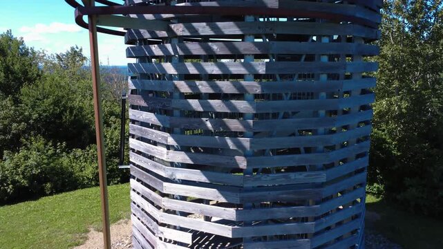 Drone footage slowly ascending the structure of an observation tower made of wooden planks and metal angle iron to its summit platform. Belvedere Coeur des Plateaux, Quebec, Canada, 2025.