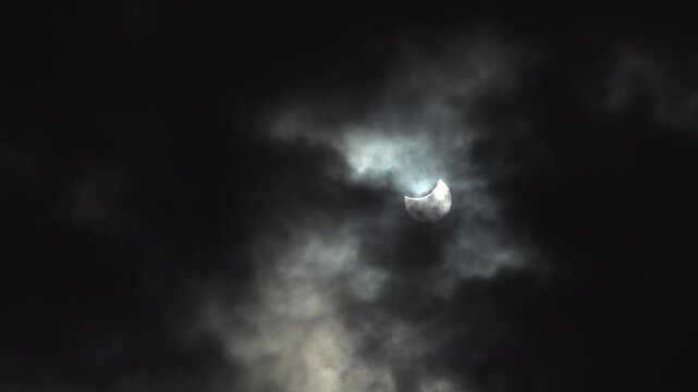 Dark clouds move across the sky with a partial solar eclipse in the background.
