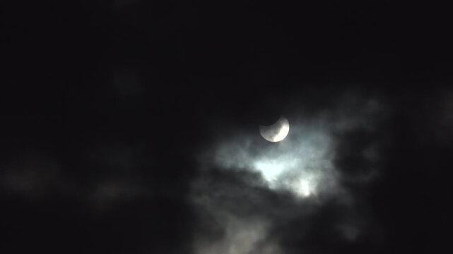 Dark clouds reveal a partial solar eclipse only to be washed out by the bright sun.