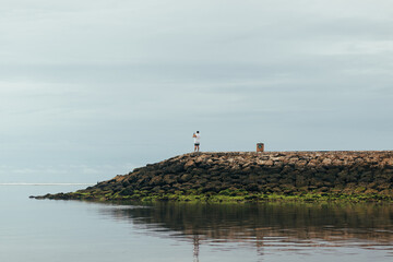Man standing on rocky breakwater by the calm sea