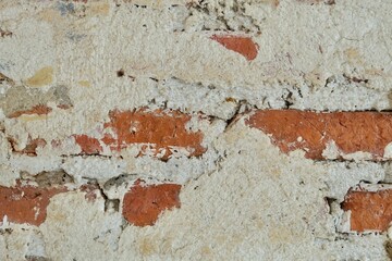 Close-up of a rugged, textured background where rough white plaster is cracking and peeling away to reveal the orange brick and mortar underneath.