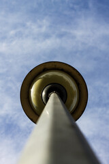 Extreme low-angle view of a yellow street lamp on a tall pole, pointing directly up into a bright, wispy blue sky, creating strong perspective and contrast.

