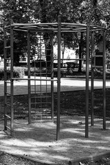Black and white image of an empty metal monkey bar and pull-up frame in an outdoor park or schoolyard, representing fitness, urban sport, and playground geometry.

