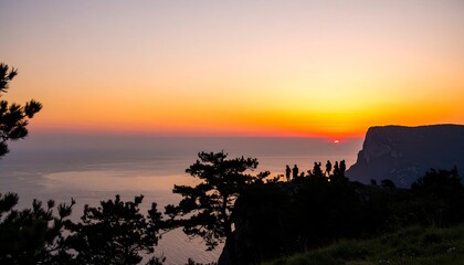 Silhouetted People Watching Sunset Over Ocean From Mountain Peak
