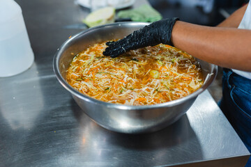 Hand with glove mixing vegetables in metal bowl