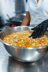 Chef mixing shredded vegetables in metal bowl with glove