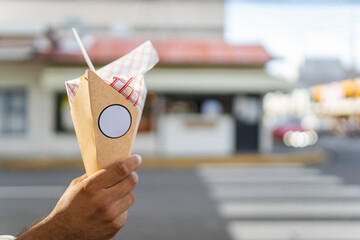 Hand holding paper cone with street food outside cafe