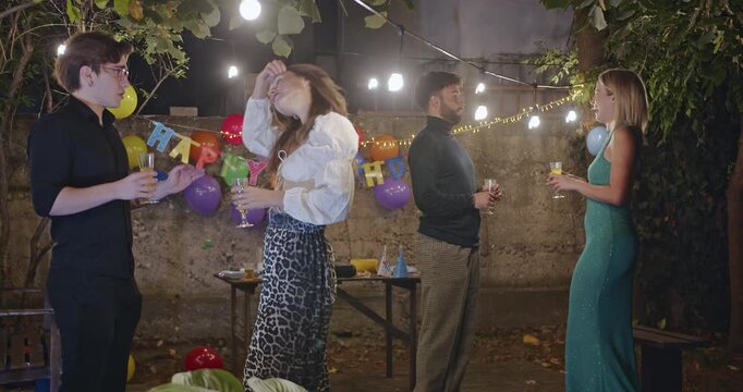 Friends enjoying drinks and conversation at an outdoor birthday party. The warm glow of string lights and colorful balloons create a festive atmosphere.