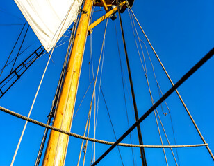Obraz premium Tall sailboat mast with rigging against a bright blue sky