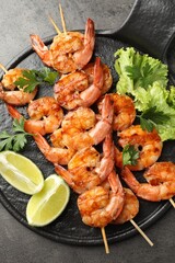 Skewers with tasty grilled shrimps, lime slices, parsley and lettuce on grey table, top view. Delicious seafood dish