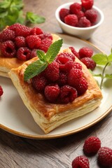 Yummy puff pastries with raspberries and mint on wooden table, closeup