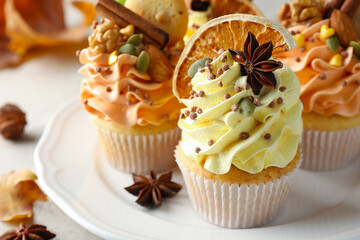 Delicious cupcakes with colorful cream, spices, cookies and nuts on table, closeup