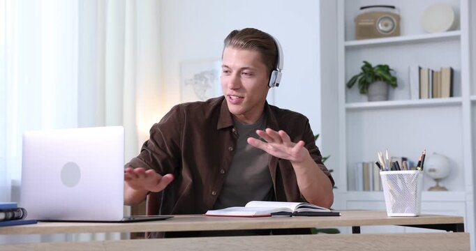 Man in headphones passing online test via laptop at table indoors