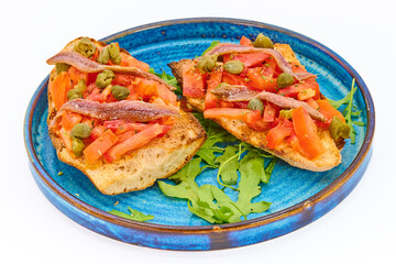 Italian bruschetta with fresh tomatoes, capers, anchovies and crusty bread on a blue plate