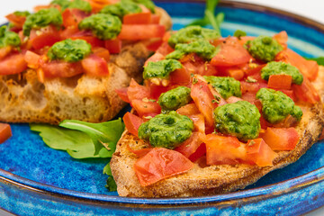 Italian bruschetta with fresh tomatoes, pesto and crusty bread on a blue plate with a white background