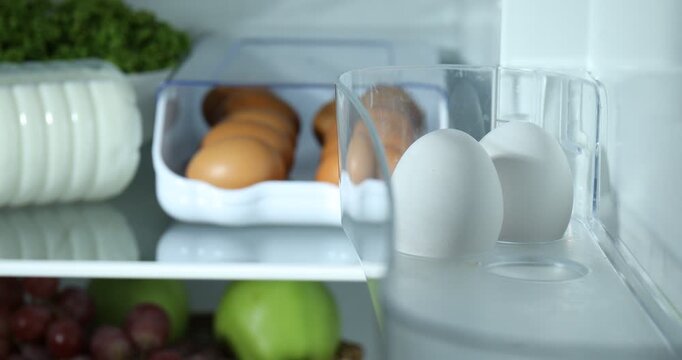 Woman putting raw chicken eggs into fridge, closeup