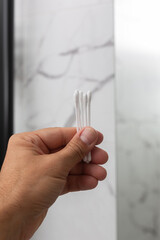 Hand holding multiple cotton swabs against a marble background, showcasing personal care items and hygiene essentials in a modern bathroom setting