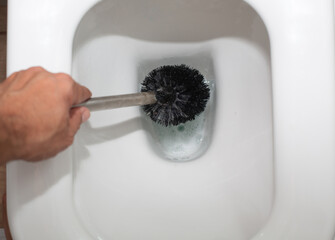 Hand holding a toilet brush, cleaning a white toilet bowl filled with water, showcasing the cleaning process and hygiene maintenance in a bathroom environment