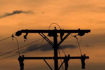 Silhouette of high voltage electric pole at sunset sky background.
