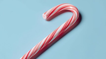 A single candy cane with red and white stripes on a light blue background in a studio setting view - Powered by Adobe