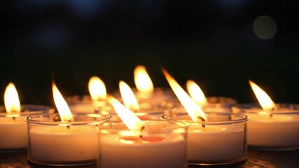 Numerous lit tea light candles arranged close together in small glass containers creating a warm glow against a dark background
