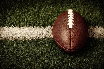Obraz premium A brown oval ball rests on a green grass field beside a white line, close-up