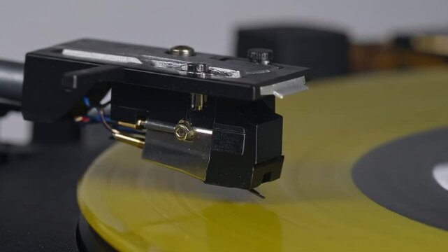Close-up of a turntable stylus tracking the grooves on a spinning, vibrant yellow vinyl record