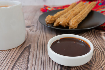 Chocolate near a plate with churros, and a cup of hot chocolate