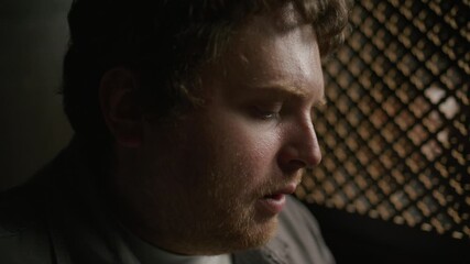 Young man talking through wooden lattice screen, confessing his sins to priest in church. Close-up view
