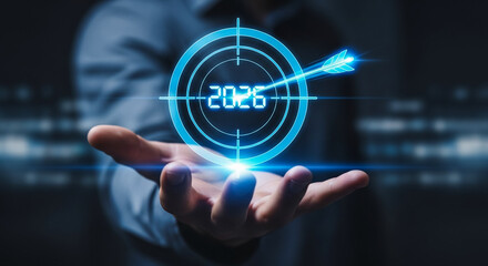 Naklejka premium A hand holding a glowing blue digital target with the year 2026 and an arrow hitting the bullseye, symbolizing future goals and achievement.