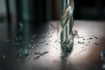 close up of drill bit drilling through a sheet of metal with some back lighting