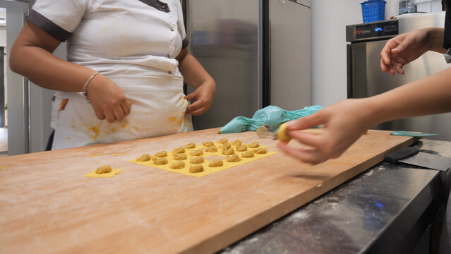 Artisan hands carefully crafting delicate tortellini pasta dough filling and folding with precision in a busy professional small business kitchen environment - Powered by Adobe