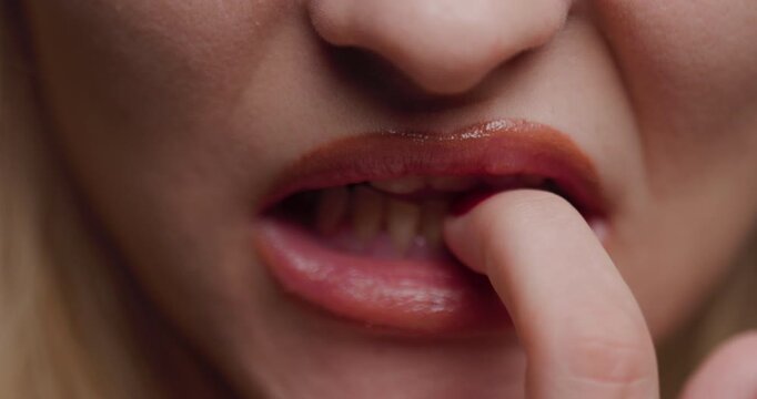Close-up of a young blonde woman's lips with a finger on them, conveying a sense of mystery